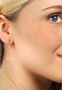 Guldstiftörhänge med en slät, rund form och en polerad yta. Nära vy som framhäver örsnibben och den omgivande hudens struktur.