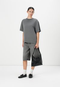Grijze oversized t-shirt, grijze denim shorts, zwarte leren tas, zwarte schoenen met strikdetail, witte sokken. Minimalistische stijl op een witte achtergrond.