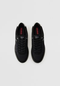 Baskets de sport noires avec une tige en textile texturé, des lacets noirs et des accents blancs contrastants au talon. Logo rouge sur les semelles intérieures.