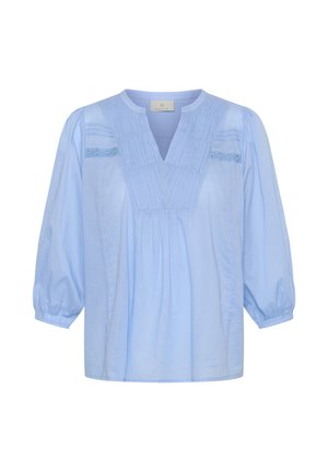 Hele sinine puuvillane pluus V-kaelusega, volditud esiosaga ja kogutud kolmeveerandsed varrukad. Rinna piirkonnas pitsdetailid.