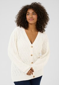 Cardigan lavorato a maglia color crema con scollatura a V, caratterizzato da una texture di motivi a onda e grandi bottoni di chiusura lungo la parte anteriore. Maniche lunghe e svasate.