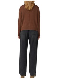 Brązowy dzianinowy sweter, lekko krótki, z prążkowanym dołem, zestawiony z luźnymi ciemnymi spodniami dżinsowymi. Widok z tyłu prezentuje luźny krój i teksturę.