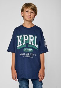 T-shirt bleu marine à manches courtes avec un grand design graphique vert et blanc portant la mention "KPRL MMIV HEART AND SOUL IN MARSEILLE."