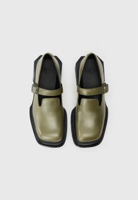 Olive zelene usnjene čevlje z zaobljenim prstom, odkrito stranjo in črnim gumijastim podplatom. Imajo sprednji trak z kovinsko sponko.