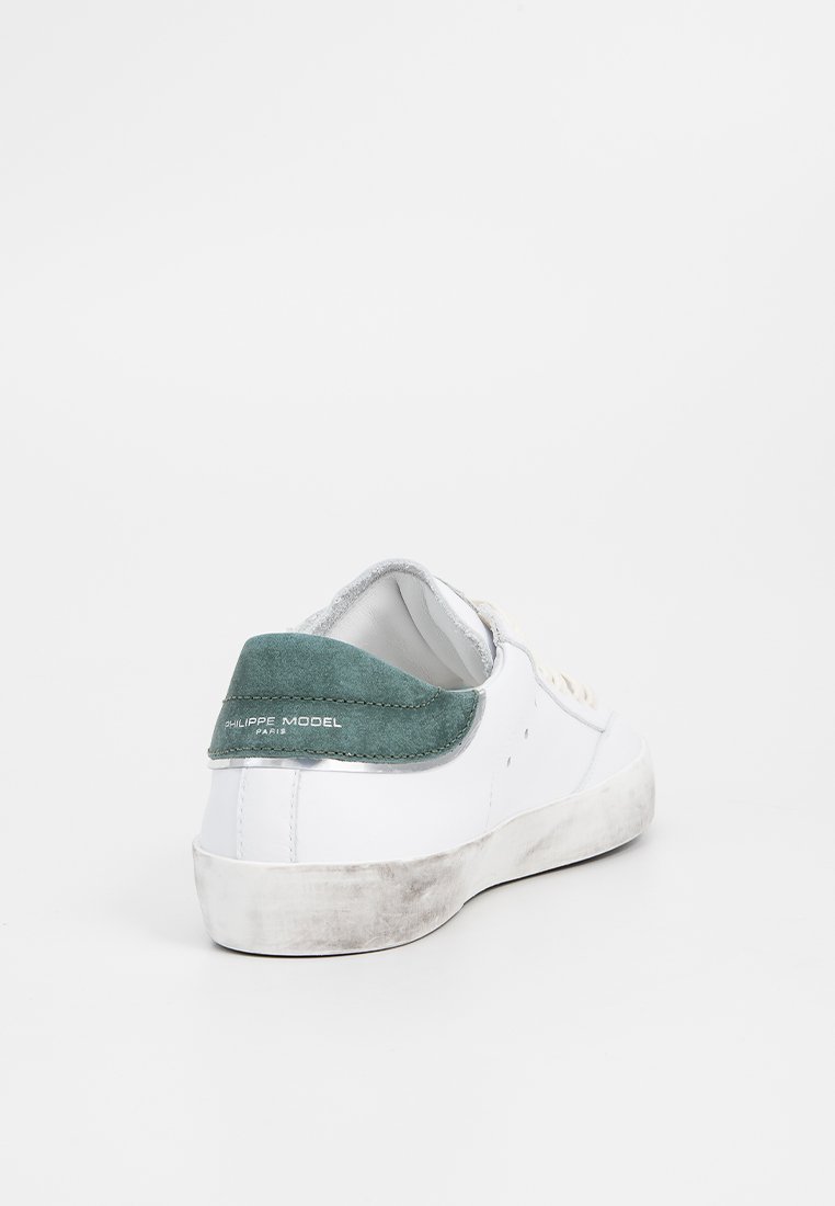 Sneaker bianco in pelle con tallone in suede verde, fodera grigia e suola bianca usurata. Presenta cuciture minimali e un marchio ridotto sul tallone.
