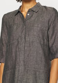 Tmavě šedá lněná košile s krátkým rukávem, límcem na knoflíky a náprsními kapsami. Disponuje texturovanou látkou a jemným prošitím.