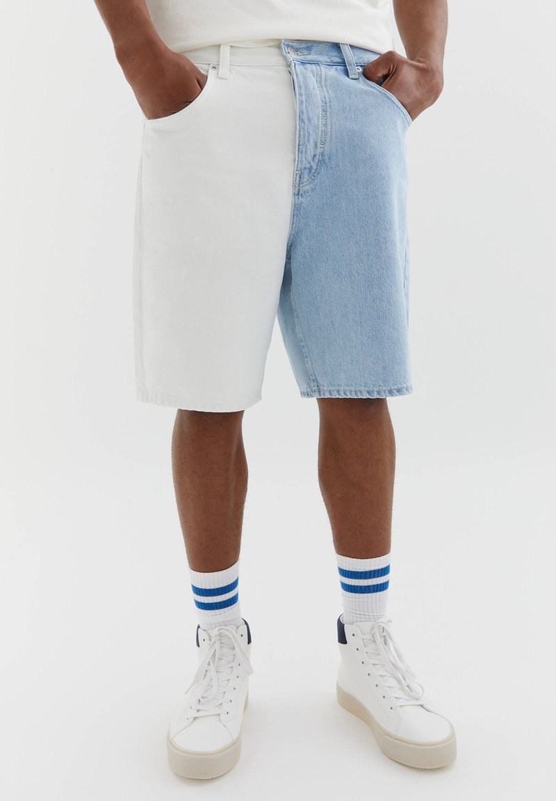 Short en jean, côté gauche blanc et côté droit bleu clair, avec une coupe décontractée. Fini avec un ourlet effiloché et des poches avant.