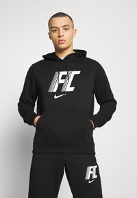 Felpa nera in misto cotone, con un grande logo bianco 'FC' e il baffo Nike. Include una tasca frontale e un cappuccio regolabile con cordini.