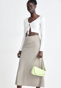 White ribbed long-sleeve crop top with front ties, paired with a light beige midi skirt. Holding a small, light green handbag.