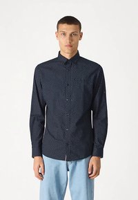 Tmavě modrá košile na knoflíky s bílým puntíkovaným vzorem, dlouhými rukávy a jednou kapsou na hrudi. Vyrobena z hladké látky.