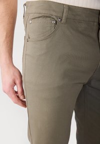 Khaki hlače iz trpežnega bombažnega materiala, z ožjim krojem, stranskimi žepki in kovinskimi dodatki. Teksturovana tkanina z gladkim zaključkom.