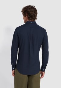 Marineblauwe lange mouwen shirt met een puntige kraag, een rugplooitje en witte knopen op de manchetten. Glad stof met een lichte glans.