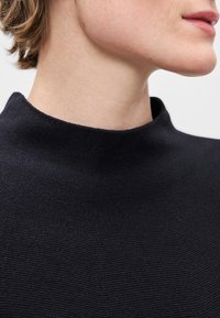 Námořnicky modrý svetr s vysokým límcem a texturovaným povrchem, s přiléhavým střihem a hladkým výstřihem. Jednoduchá a minimalistická konstrukce.