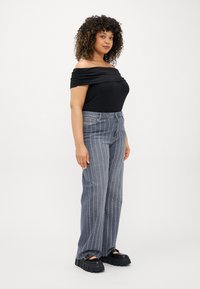 Top preto sem alças com tecido drapeado, combinado com jeans cinza de risca de giz de perna larga. Sapatos plataforma pretos completam o visual.