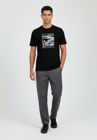 Musta lyhythihainen t-paita, jossa on harmaalla "KARL" ja "LAGERFELD" -tekstillä varustettu graafinen painatus; yhdistetty harmaisiin housuihin ja mustiin lenkkareihin.