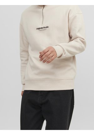 Sudadera beige con cuello con cremallera, que presenta un logo en el pecho en negro. Fabricada con tejido suave, cuenta con puños y dobladillo de canalé.