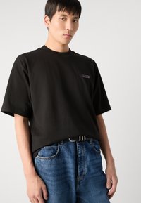 Tricou din bumbac negru cu mâneci scurte, cu un logo pe pieptul stâng. Purtați cu blugi din denim albaștri și o curea în dungi alb-negru.