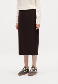 Jupe mi-longue marron en tissu doux, associée à des baskets grises et beige avec un motif texturé et une semelle en caoutchouc.
