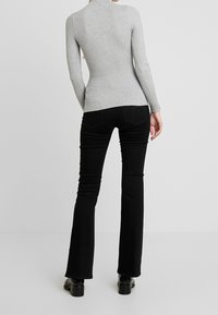 Pull gris à col roulé côtelé, coupe ajustée, manches longues, associé à un jean noir évasé. Détails remarquables sur les poches arrière. Bottines noires.