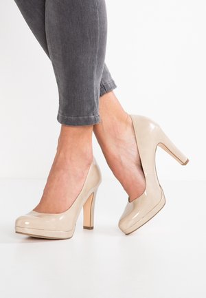 Beige laklæder højhælede sko med rundet tå, skjult plateau og chunky hæl, kombineret med grå ankellange jeans.