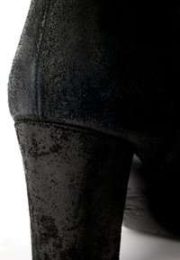 Gros plan d'une chaussure à talon haut en daim noir montrant la surface texturée et la zone arrière du talon.
