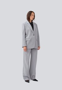 Light gray tailored suit featuring a single button blazer with notch lapels and wide-leg trousers, layered over a black shirt.