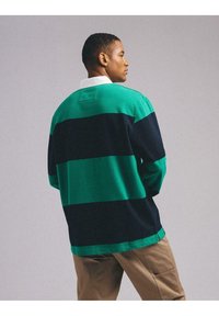 Zielona i granatowa w paski koszula z długim rękawem z kołnierzykiem, wykonana z teksturowanej tkaniny i z prostokątną naszywką na plecach. Luźny krój z bocznymi rozcięciami.