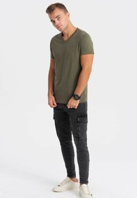 Olivengrøn v-hals t-shirt kombineret med sorte cargo-bukser og cremefarvede sneakers, med en tætsiddende pasform og glat tekstur. Casual design med minimale detaljer.