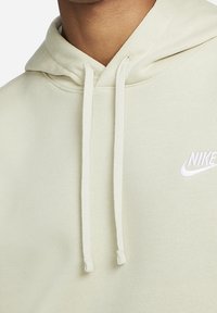 Ljusgrön hoodie i mjukt tyg med känguruficka, dragsko i huvan och vitt broderat logotyp på vänster bröst.