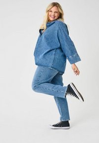 Ensemble en denim avec une veste bleue ample et un jean bleu ajusté, complété par des baskets noires montantes. Le tissu semble texturé et décontracté.