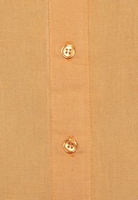 Light orange linen shirt featuring a close-up of a button placket with two round, golden buttons and a subtle textured fabric.