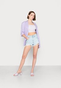 Blazer oversized lavanda sobre um top cropped branco xadrez e calções de ganga azul claro com efeitos de desgaste, combinado com mules de salto bloco em lavanda.