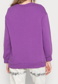 Sudadera morada hecha de material suave, con cuello redondo, mangas largas y un ajuste relajado con puños y dobladillo acanalados.