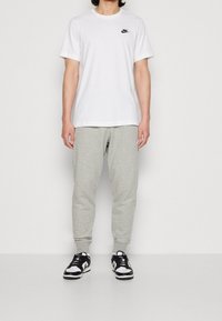White cotton t-shirt with black logo, grey fleece joggers, and black and white sneakers. Loose fit, round neckline, and ribbed cuffs.
