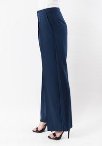 Pantaloni a gamba larga navy realizzati in tessuto morbido, con pieghe frontali, vita alta e abbinati a sandali neri con tacco.