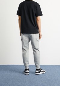 Svart bomullströja, grå cargobyxor i sweatpantsmodell med sidofickor, och svarta Nike-sneakers; fotograferat bakifrån mot en ljus bakgrund.