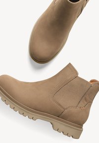 Une paire de bottes Chelsea en cuir marron clair avec des panneaux latéraux élastiques et des semelles en caoutchouc robustes, présentées en vues de dessus et de côté.