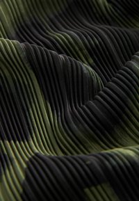 Tejido texturizado con profundos pliegues verticales en negro y tonas de verde, mostrando un patrón ondulado y una textura suave y lisa.