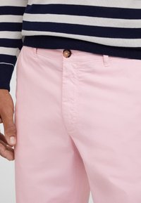Lichtroze katoenen broek met een gladde textuur, voorzien van een knoopsluiting en zijzakken, gecombineerd met een navy en wit gestreept trui.