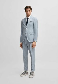 Completo a quadri azzurro chiaro con rever a notched, due tasche frontali e chiusura a un bottone, abbinato a sneakers grigie e una cravatta blu navy.