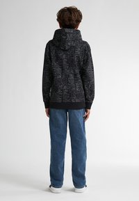 Sudadera negra cubierta de patrones abstractos de texto, con un bolsillo canguro y capucha con cordón, combinada con jeans de color azul claro.