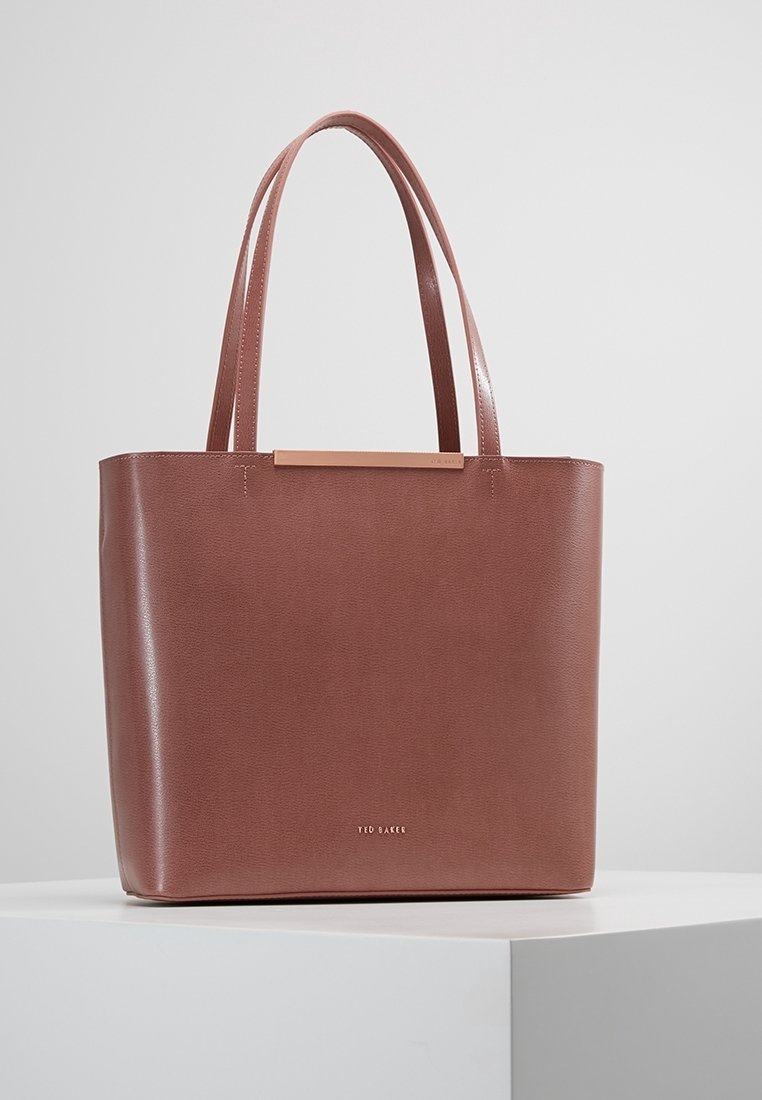 Sac cabas en cuir marron Ted Baker avec double bandoulière et logo minimaliste doré sur une surface blanche.