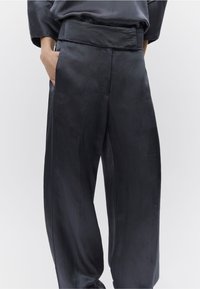 Σκούρο γκρι παντελόνι με ευρύ πόδι από απαλό, ρέον ύφασμα. Διαθέτει ψηλή μέση και μπροστινές τσέπες, με διακριτική γυαλάδα.