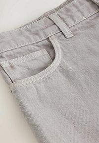 Gros plan sur un jean en denim gris clair montrant la ceinture, les passants de ceinture, la poche avant et les détails des coutures de la poche à monnaie.