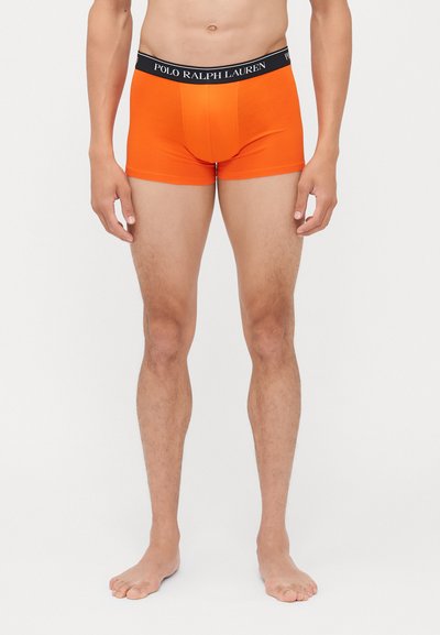 Oranžinės apatinės kelnaitės su juoda juosta, ant kurios užrašyta "POLO RALPH LAUREN." Dizainas yra prigludęs, o medžiaga atrodo lygi ir elastinga.