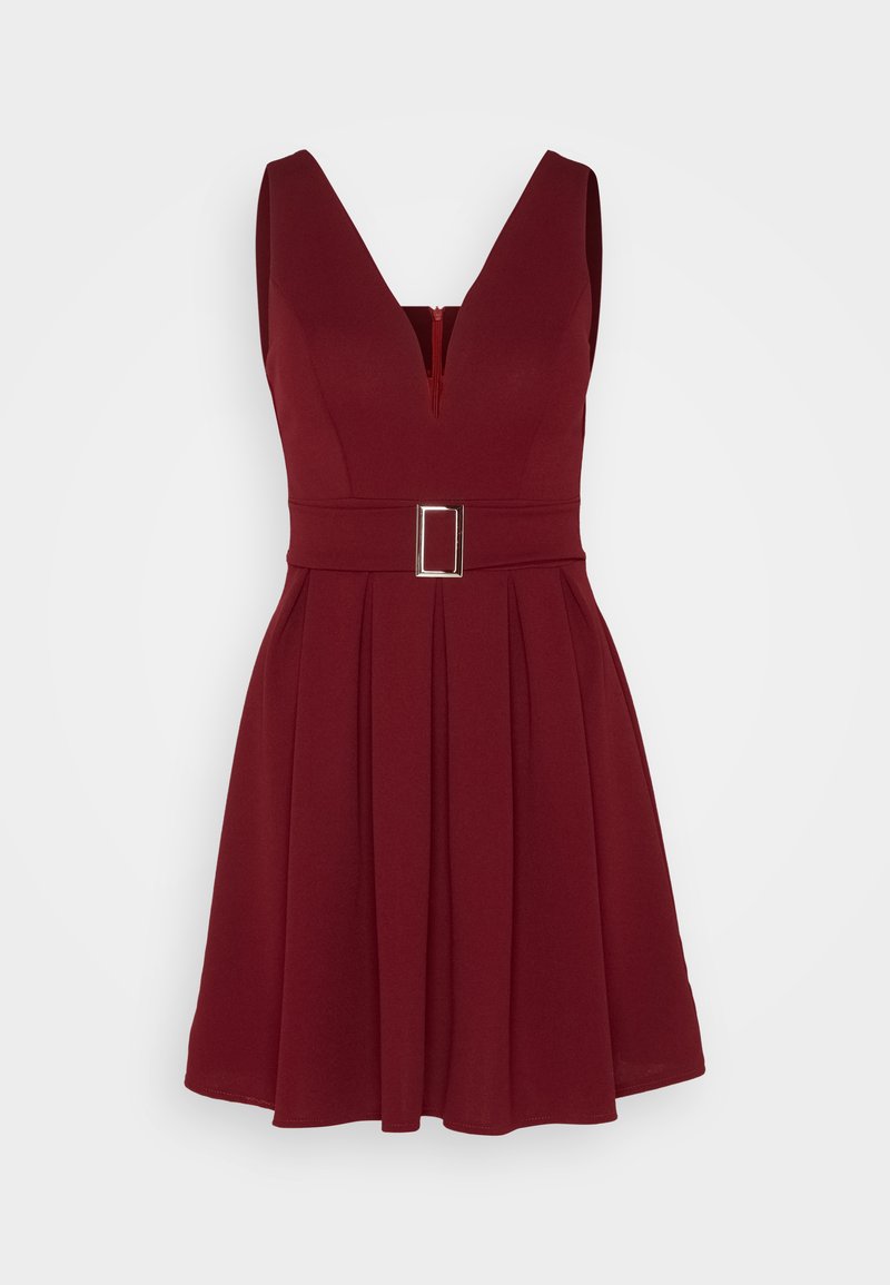 Red sleeveless dress with a V-neck and a fitted waist, featuring a rectangular belt buckle and pleated skirt. Smooth fabric texture.