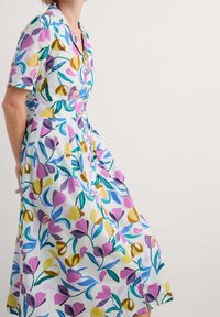 Bloemen midi-jurk van lichtgewicht stof met een combinatie van paarse, gele en blauwe bloemen met groene bladeren op een witte achtergrond.