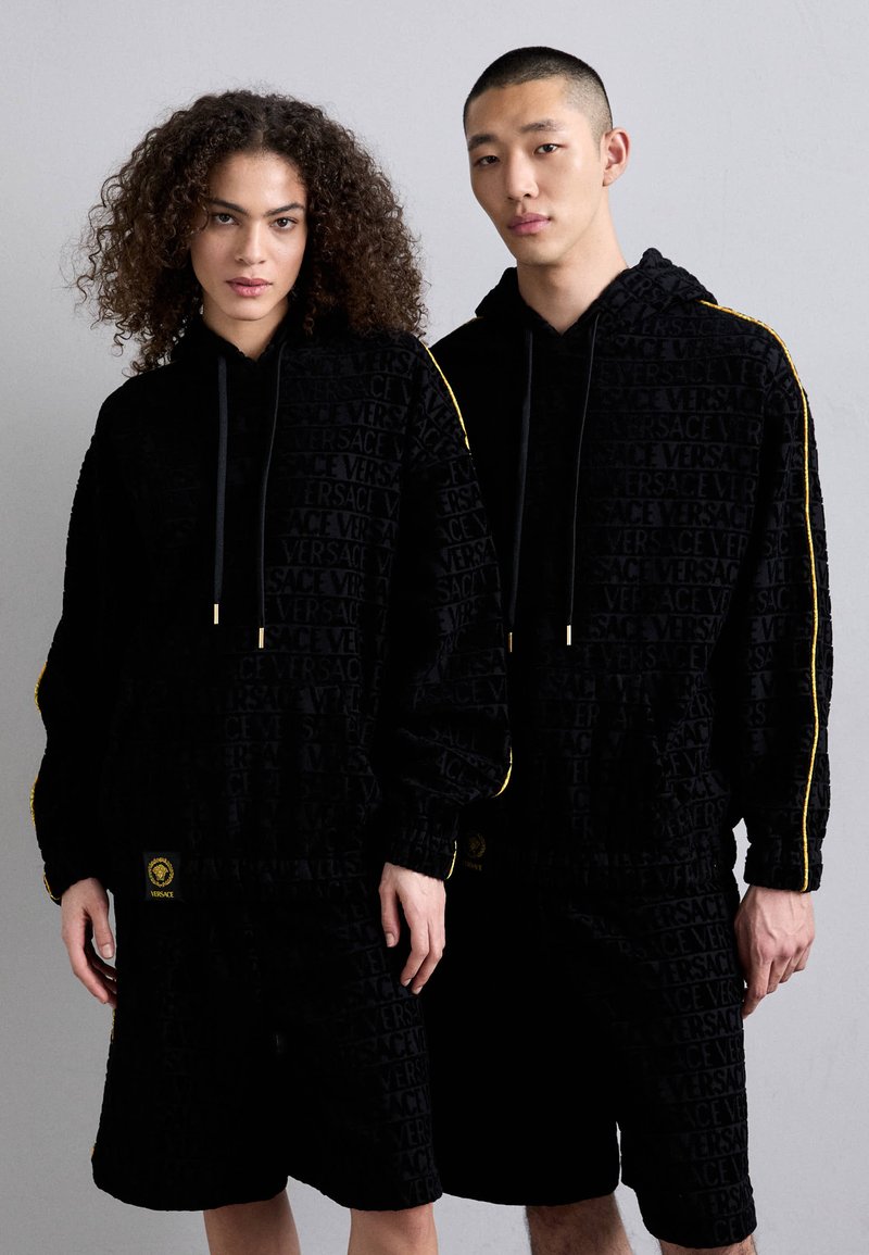 Felpe nere con design in rilievo, dotate di strisce gialle lungo le maniche. Accompagnate da pantaloni corti neri abbinati, con dettagli del logo.