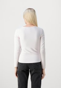 Langermet, lys rosa topp med rund hals. Jevnt teksturert med tettsittende design, kombinert med mørke, avslappede jeans.