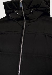 Schwarz gepolsterte Jacke mit hohem Kragen, durchgehendem Reißverschluss und horizontalen Steppdetails. Glattes, glänzendes Material ohne Muster.